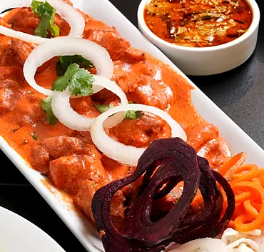 Chicken in creamy orange gravy with onion rings, coriander and beetroot garnish