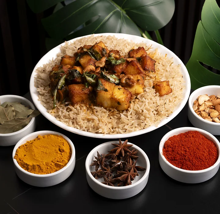Plate of mandi rice topped with spiced paneer and curry leaves, with small bowls of bay leaves, turmeric, star anise, chilli powder and cashews