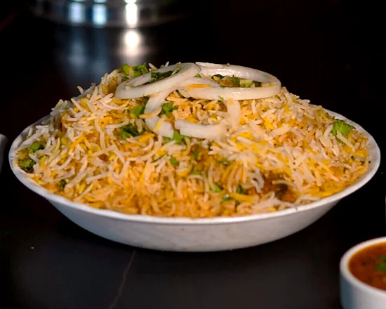 Bowl of biryani topped with onion rings, served with raita and salan